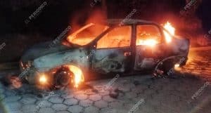 Incendio de un coche en la calle durante la noche, con llamas y humo saliendo del vehículo, en un entorno oscuro y desolado.