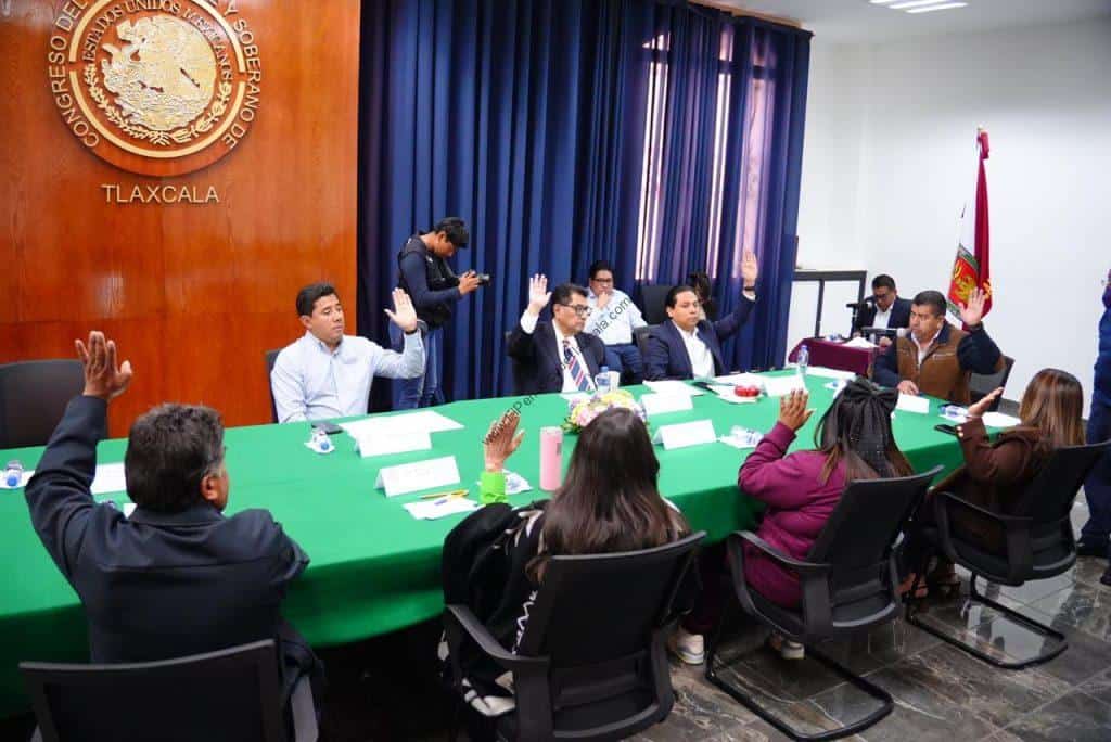 Reunión oficial en Tlaxcala con funcionarios y representantes en una sala de conferencias con bandera y escudo del estado.