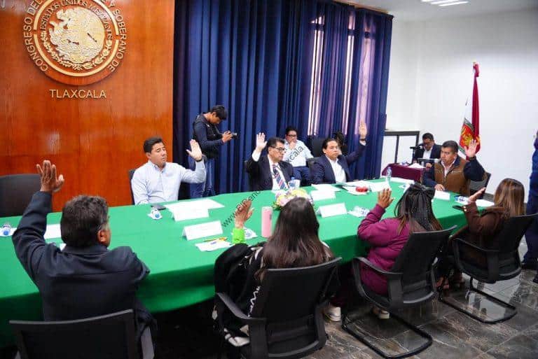 Reunión oficial en Tlaxcala con funcionarios y representantes en una sala de conferencias con bandera y escudo del estado.