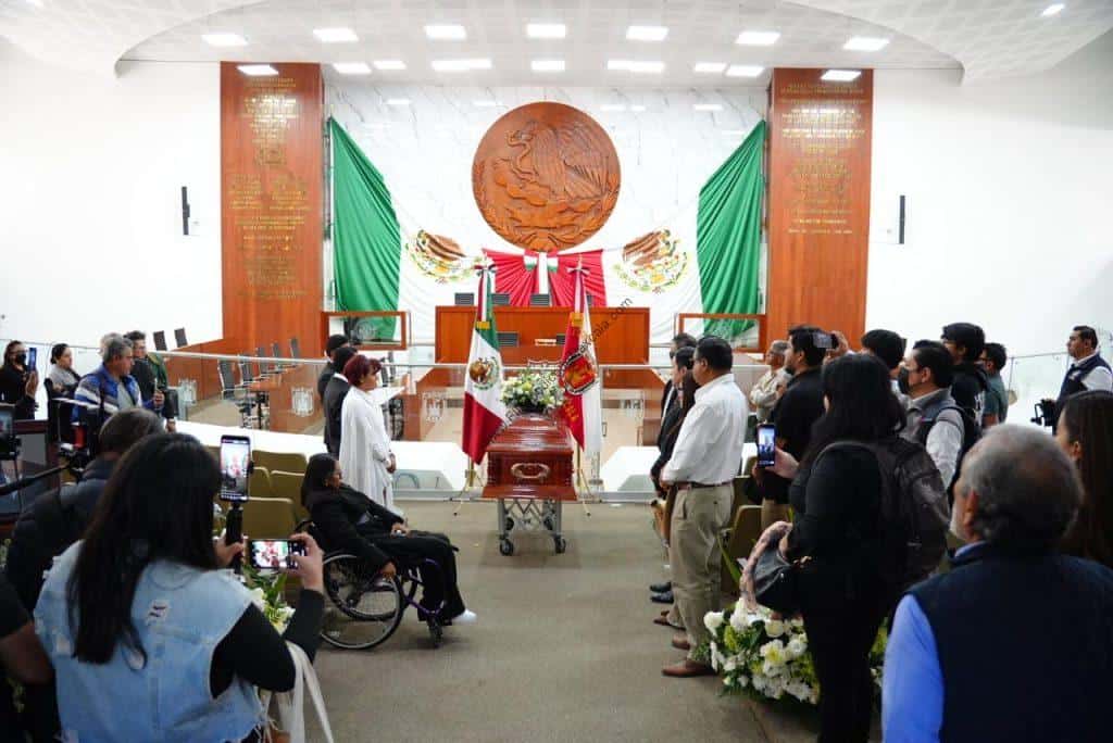 Reunión oficial en un salón con presencia de autoridades y asistentes, en un acto formal con banderas y decoraciones patrióticas en el fondo.