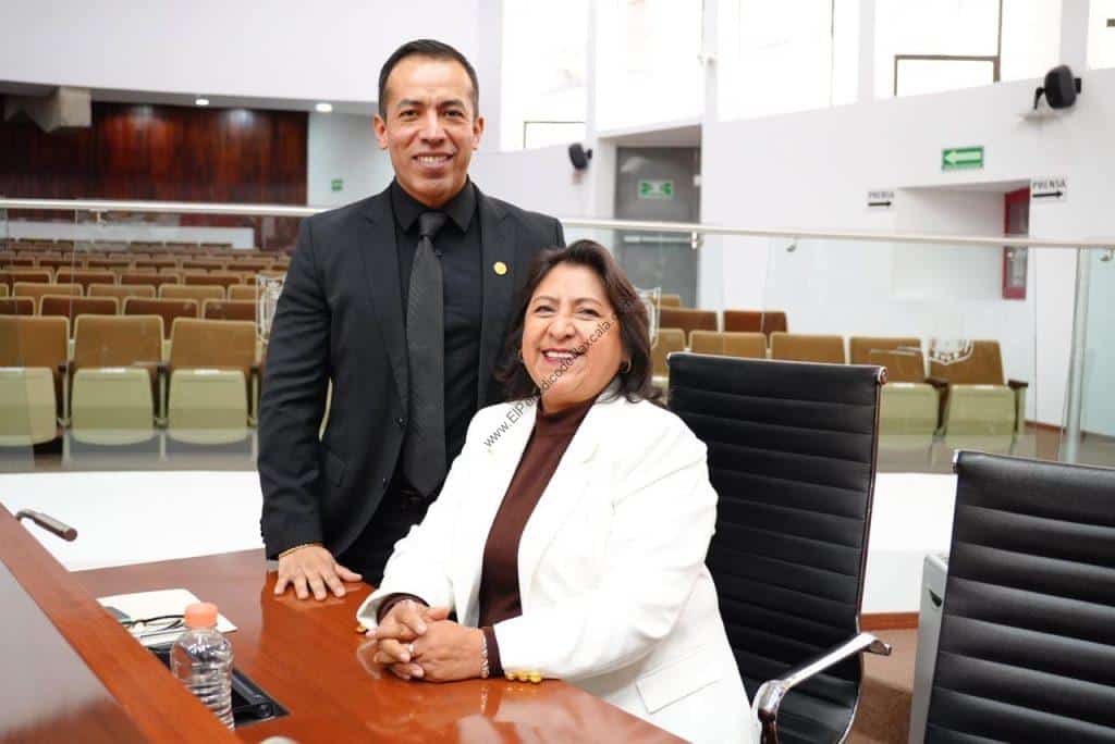 Persona en una reunión formal en un auditorio moderno, con asientos y ventanas grandes, en un entorno profesional y corporativo.