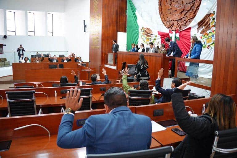 Sesión en el Congreso de Tlaxcala con legisladores participando y levantando la mano en debate sobre temas políticos y sociales.