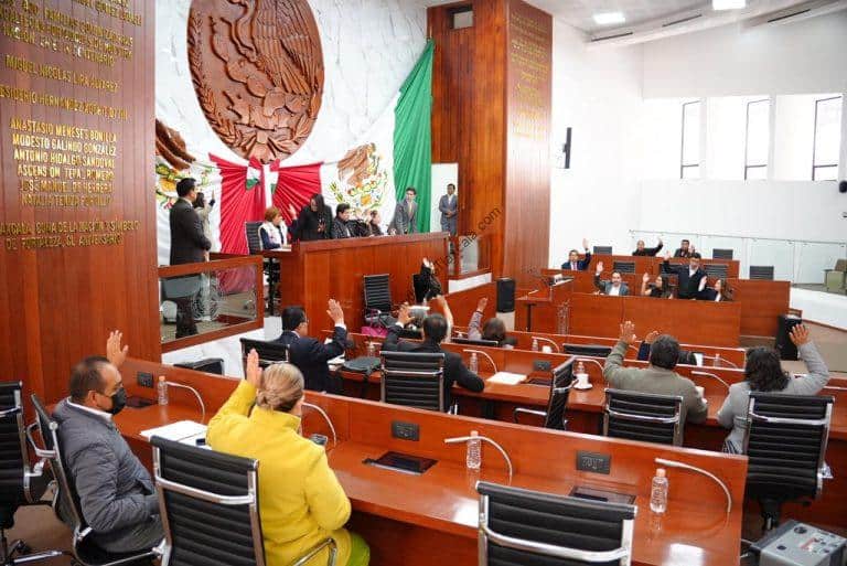 Imagen de una sesión en el Congreso de Tlaxcala con legisladores levantando la mano durante una votación oficial.