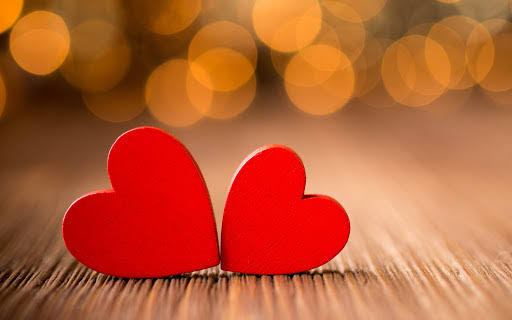 Ampliamente, 2 corazones de fieltro rojos en una superficie de madera con fondo difuso de luces cálidas, simbolizando amor y romanticismo.