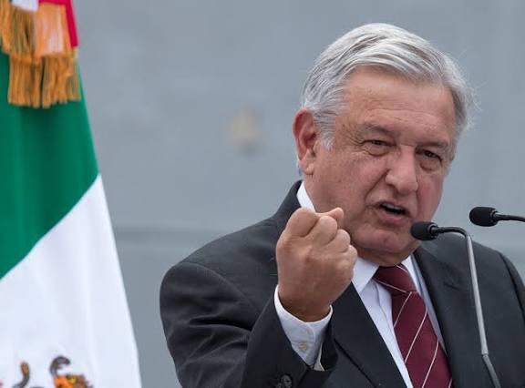 Un hombre mayor con cabello gris, vestido con traje oscuro y corbata, hablando en un micrófono con una expresión de determinación y fuerza, gesticulando con el puño cerrado, en un evento oficial con b.