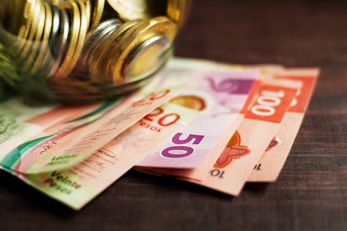 Monedas y billetes de peso mexicano en una mesa de madera, representando finanzas y economía en México.