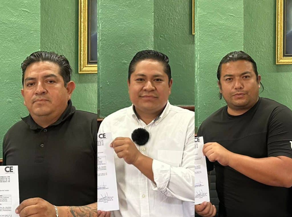 Tres hombres en una sala con paredes verdes, sosteniendo documentos y mostrando una actitud seria y confiada.