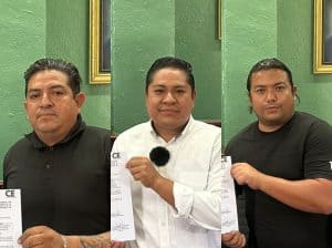 Tres hombres en una sala con paredes verdes, sosteniendo documentos y mostrando una actitud seria y confiada.