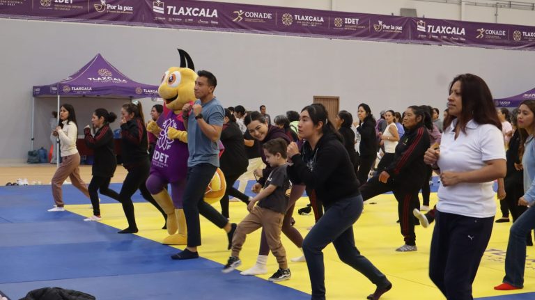 Disfraz de unicornio morado en evento deportivo con niños y adultos participando en una actividad en un gimnasio cubierto.