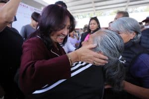 Mujer sonriendo y abrazando a una persona mayor en un evento comunitario en Tlaxcala, México.