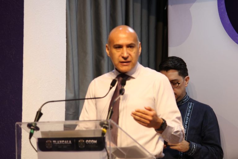 Hombre hablando en un podio durante una conferencia o evento formal en un entorno interior.