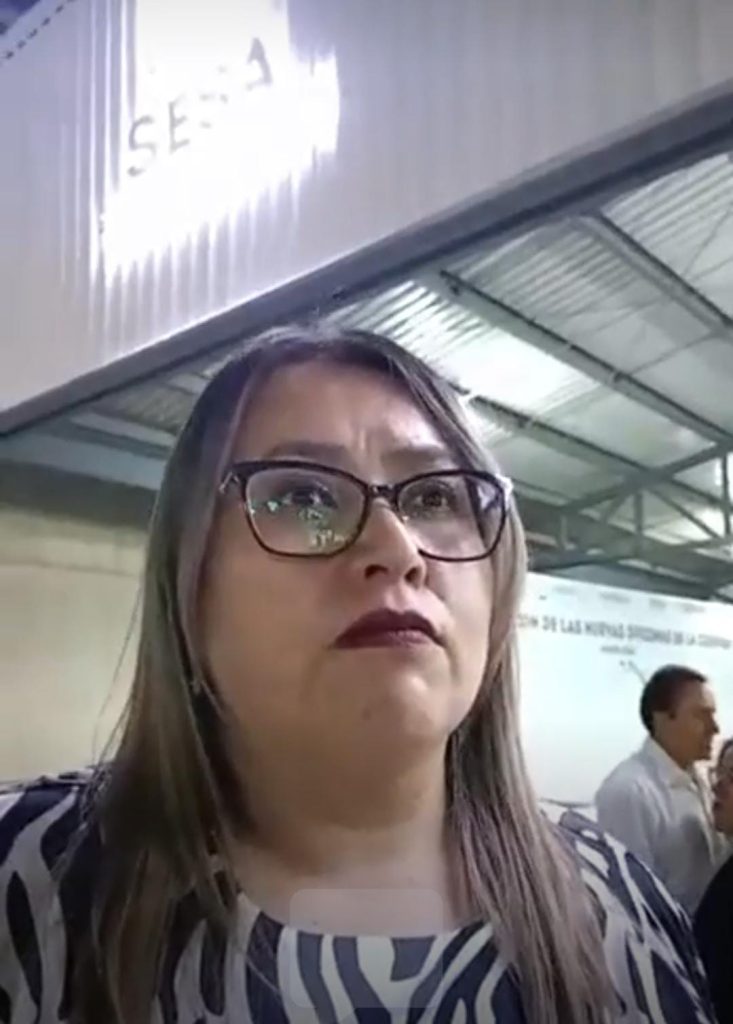 Mujer con gafas y cabello largo en un entorno de interior, posiblemente en un evento o conferencia en Tlaxcala, México.