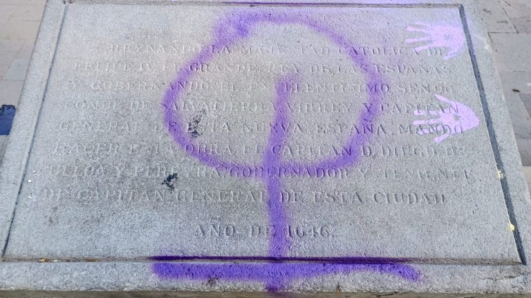 Haga clic en la imagen para ampliar la vista y observar los detalles del texto en la placa con grafiti morado en la superficie de piedra.