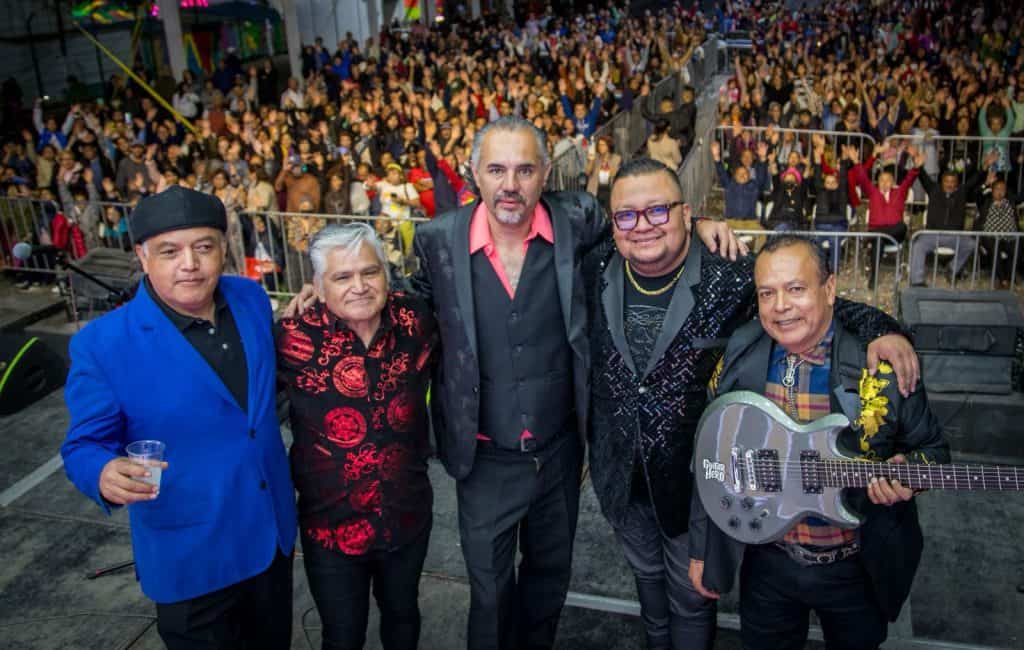 Un grupo de cinco músicos en un concierto en vivo, con una multitud de espectadores en el fondo, en un evento cultural en Tlaxcala, México.
