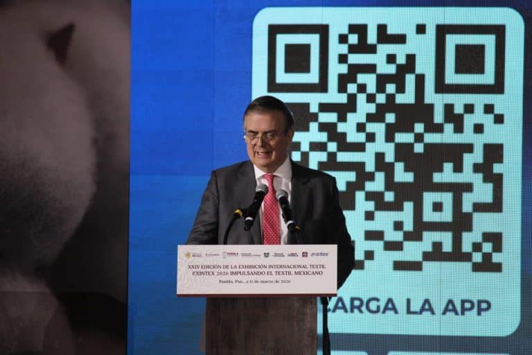Código QR para descarga de la app en una conferencia, con un hombre vestido con traje y corbata hablando en un podio.