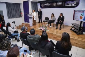 Personas participando en una conferencia o evento oficial en un salón, con un panel de discusión y una audiencia atenta, en un entorno formal y profesional en Tlaxcala.