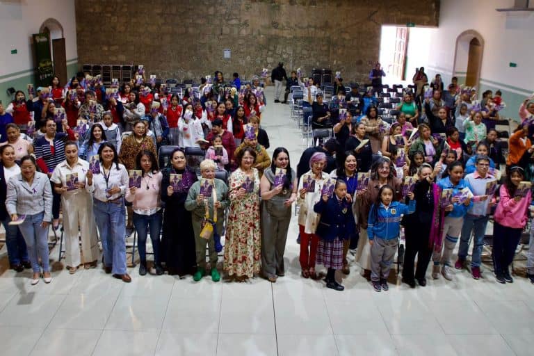 Gran grupo de personas, incluyendo niños y adultos, reunidas en un evento en un salón amplio con paredes de color claro y ventanas grandes que dejan entrar luz natural.