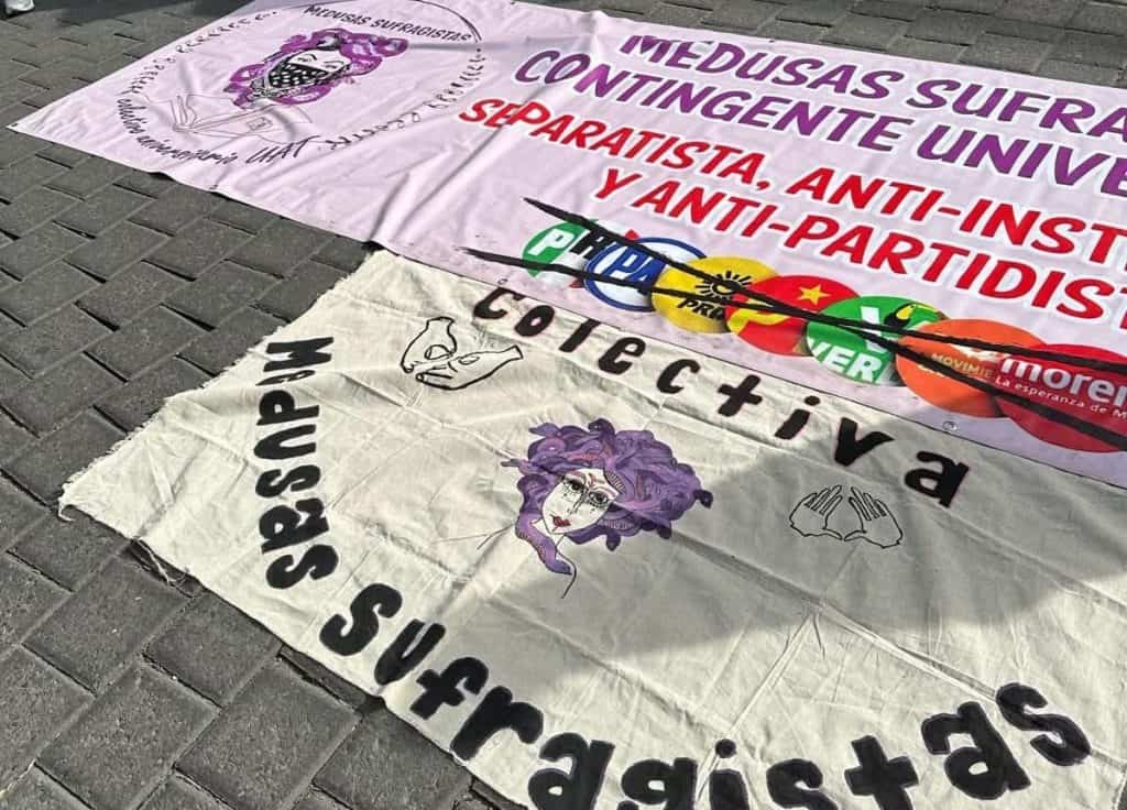 Banderas y pancartas en una manifestación contra la violencia y el autoritarismo en Tlaxcala, México, con mensajes de resistencia y lucha social en el suelo.