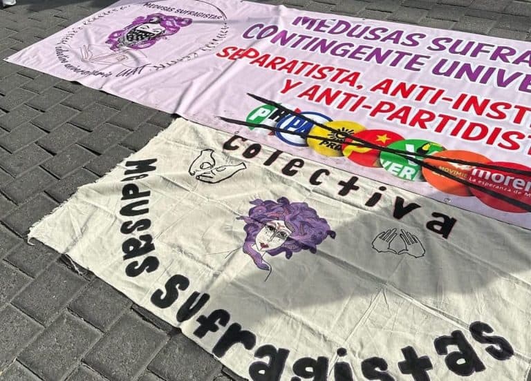 Banderas y pancartas en una manifestación contra la violencia y el autoritarismo en Tlaxcala, México, con mensajes de resistencia y lucha social en el suelo.