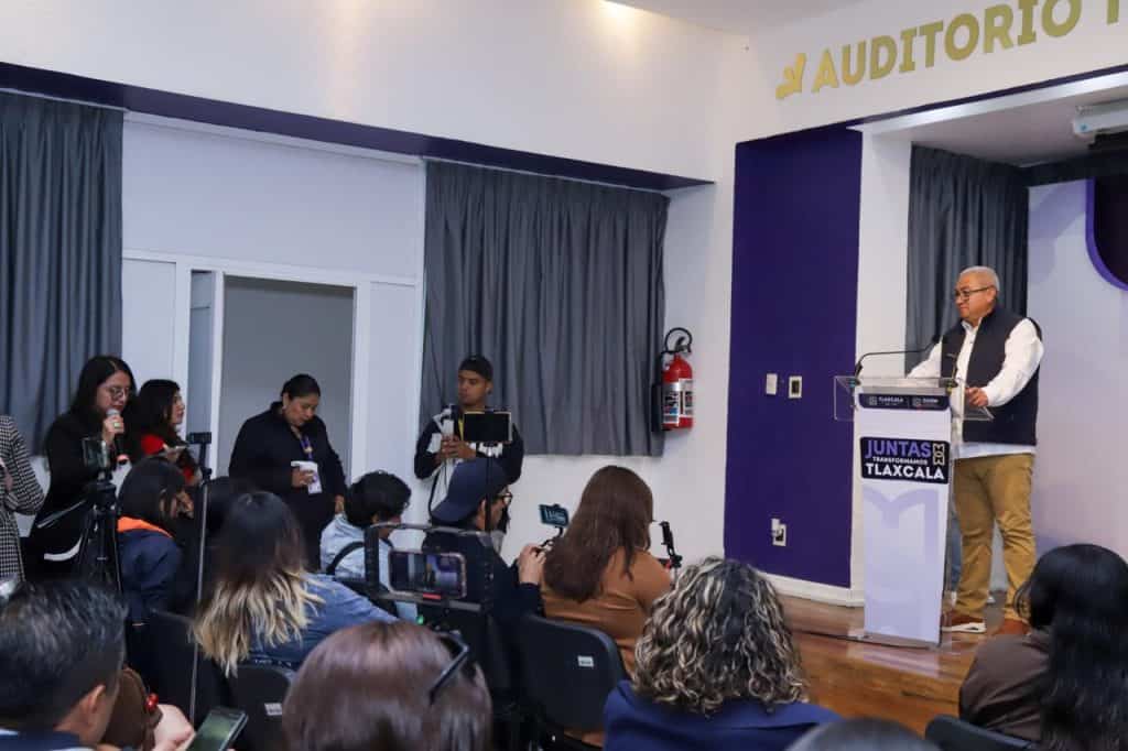 Persona dando una conferencia en un auditorio con audiencia y periodistas presentes, en Tlaxcala, México.