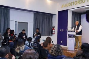 Persona dando una conferencia en un auditorio con audiencia y periodistas presentes, en Tlaxcala, México.