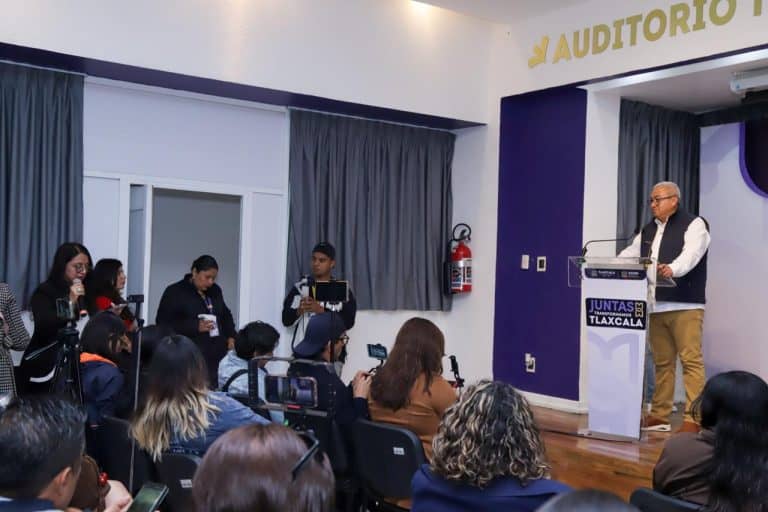 Persona dando una conferencia en un auditorio con audiencia y periodistas presentes, en Tlaxcala, México.