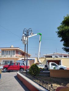 Reparación de luminarias públicas en una calle de Tlaxcala, con un camión de trabajo elevado y un técnico realizando mantenimiento en un poste de luz.