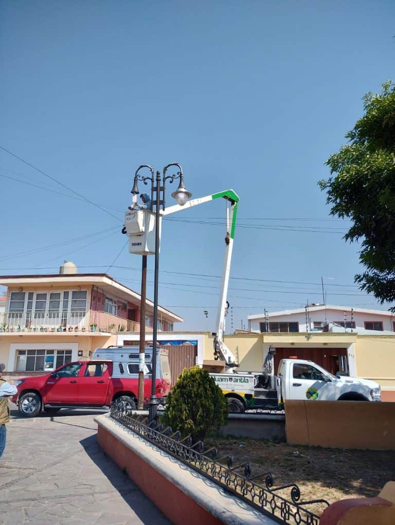 Reparación de luminarias públicas en una calle de Tlaxcala, con un camión de trabajo elevado y un técnico realizando mantenimiento en un poste de luz.