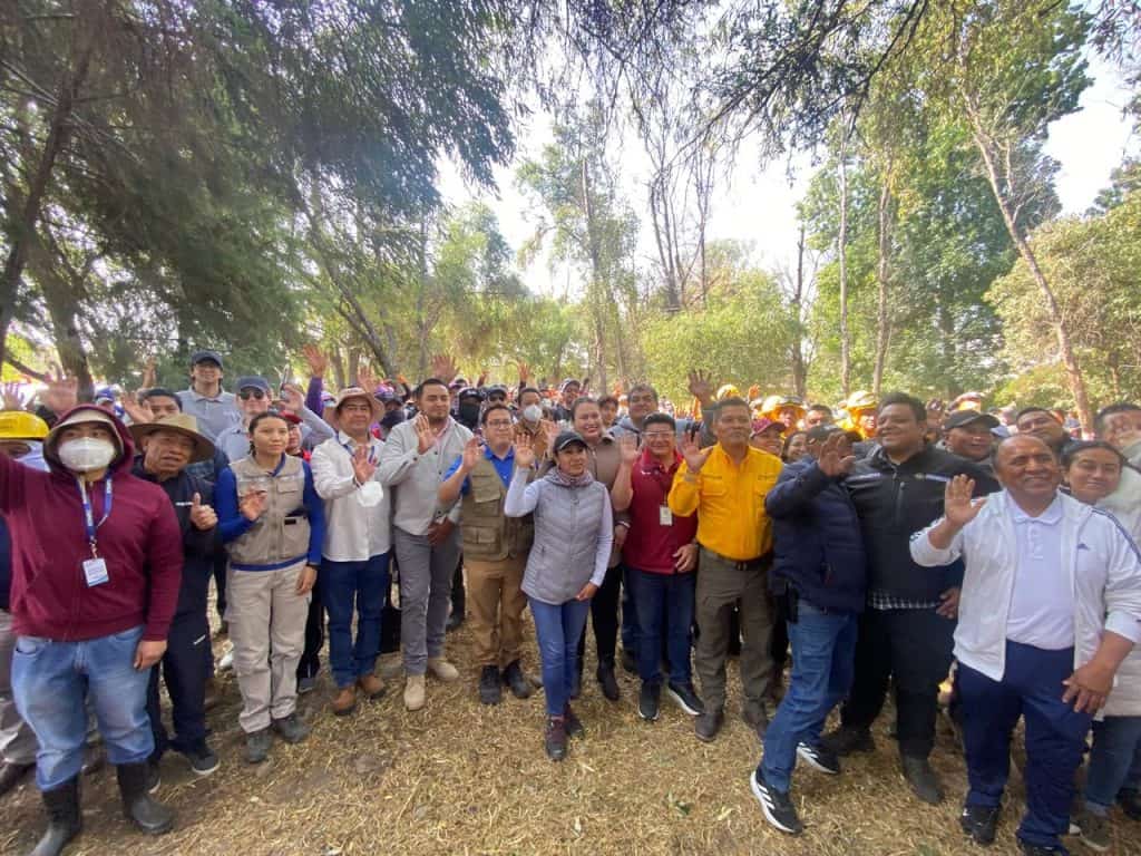 Cientos de personas reunidas en un espacio al aire libre, participando en un evento comunitario en Tlaxcala, México, con árboles y naturaleza de fondo, en un día soleado.