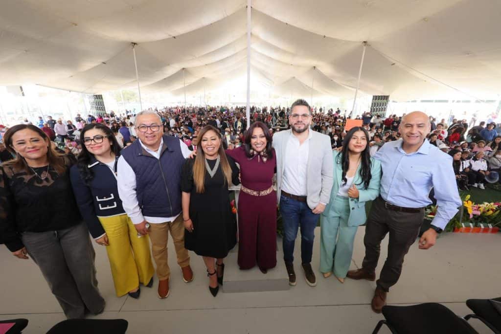 Personas en un evento bajo una gran carpa, posando para la foto con una multitud de fondo.