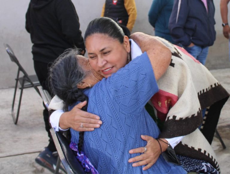 Mujer mayor y mujer joven se abrazan con alegría en un encuentro emotivo al aire libre.
