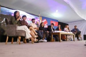 Aprendizaje y discusión en un panel con varios jóvenes en un evento cultural en Tlaxcala, México, con fondo de banderas y pantallas digitales.