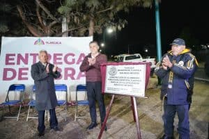 Personas en ceremonia de inauguración de obra pública en Tlaxcala, con un cartel que indica la entrega de obra en San Diego Metepec durante la noche.