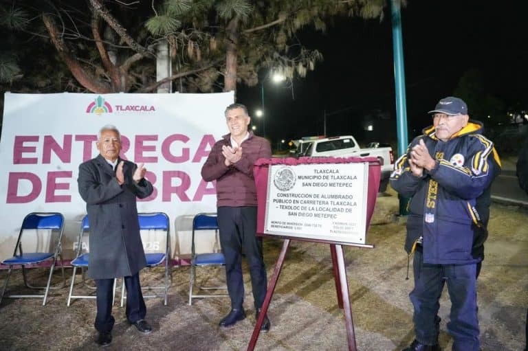 Personas en ceremonia de inauguración de obra pública en Tlaxcala, con un cartel que indica la entrega de obra en San Diego Metepec durante la noche.