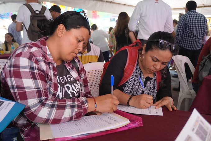 Estudiantes llenando formularios en una mesa durante un evento al aire libre en Tlaxcala, México, con varias personas en el fondo participando en la actividad.