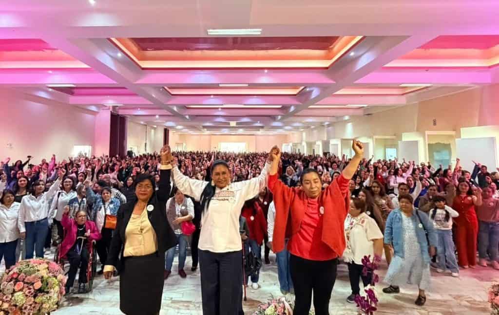 Personas celebrando en un evento masivo en un salón con iluminación rosa y techo decorado, con muchas personas en el fondo participando en la celebración.