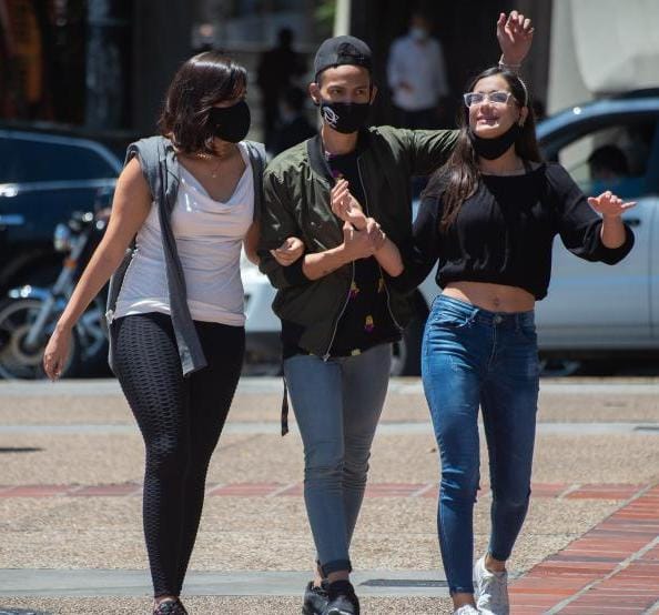 Personas jóvenes caminando juntas en la calle, usando mascarillas y disfrutando del día.