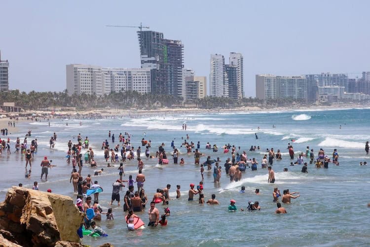 Playa concurrida con muchas personas disfrutando del mar y el clima cálido en un día soleado en la ciudad costera.
