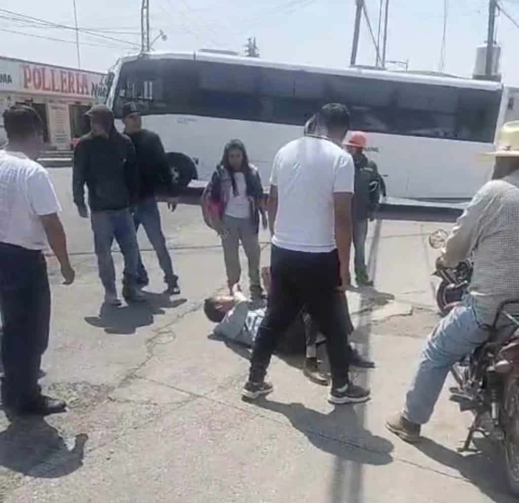 Persona siendo atendida en la calle tras un accidente, rodeada de varias personas y un autobús en el fondo, en una zona urbana de Tlaxcala.