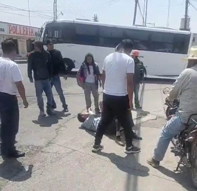 Persona siendo atendida en la calle tras un accidente, rodeada de varias personas y un autobús en el fondo, en una zona urbana de Tlaxcala.