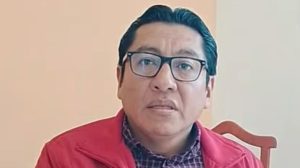Hombre con gafas y chaqueta roja en una entrevista o reunión, sentado en una habitación con fondo neutro.