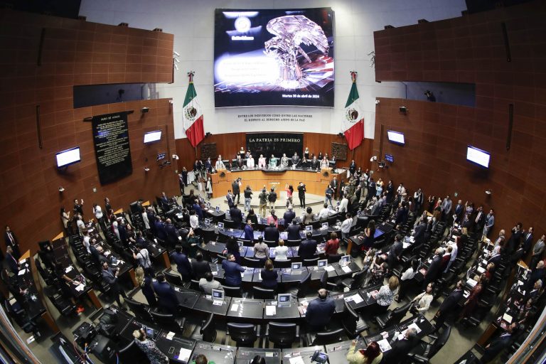 La imagen muestra una sesión del Congreso de México con legisladores y asistentes en un auditorio grande, con banderas mexicanas y pantallas que muestran información relevante.
