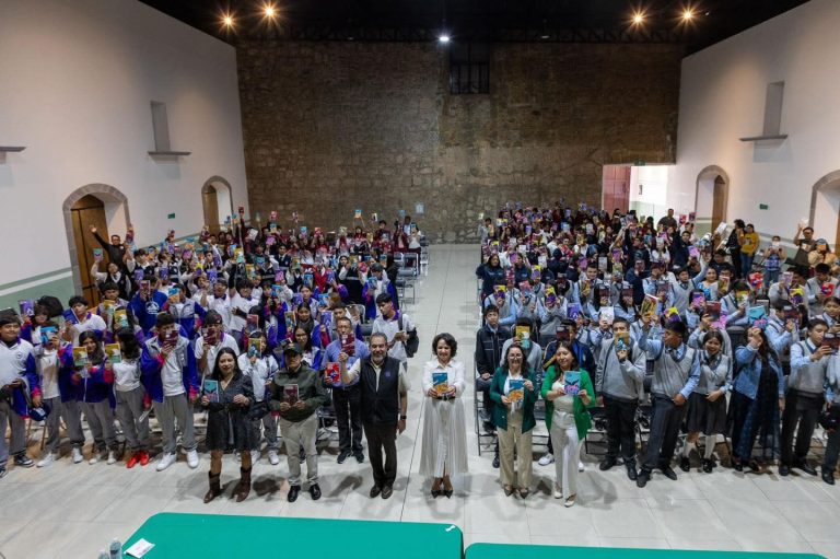 Personas reunidas en un evento en un salón amplio, con algunos en el escenario y otros en las mesas, en un ambiente formal y festivo.