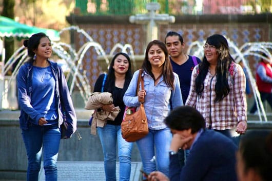 Grupo de jóvenes sonriendo y caminando en un parque con fuentes y fondo de árboles, disfrutando del día al aire libre en Tlaxcala, México.