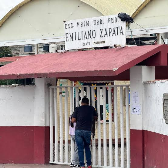 Escuela primaria Emiliano Zapata en Tlaxcala, México, con estudiantes y un adulto en la entrada, mostrando un ambiente escolar en una comunidad local.