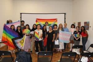 Orgullo LGBTQ+ en una reunión grupal con banderas y pancartas de colores en un espacio interior.