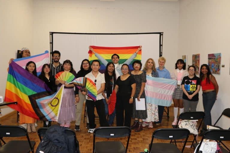 Orgullo LGBTQ+ en una reunión grupal con banderas y pancartas de colores en un espacio interior.