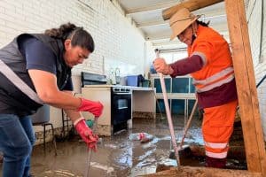 Desastre por inundación en Tlaxcala, personas limpiando agua y lodo en un espacio cerrado afectado por las lluvias intensas.