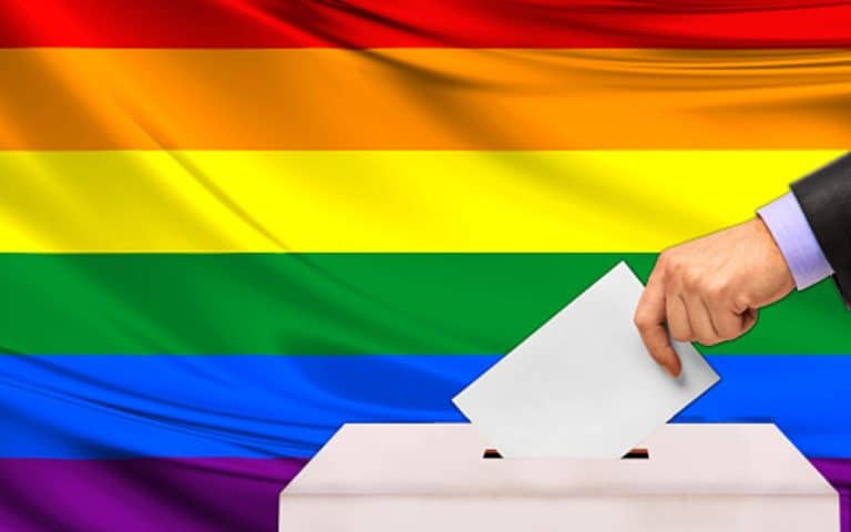 Voto en una urna con bandera del arcoíris, símbolo del orgullo LGBTQ+ en un contexto de participación electoral.