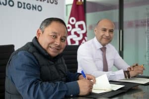 Hombre sonriendo firmando documentos en una reunión formal en una oficina moderna.